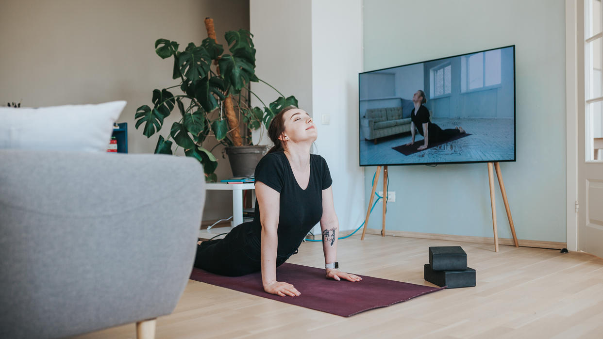  Woman practising yoga in front of TV. 