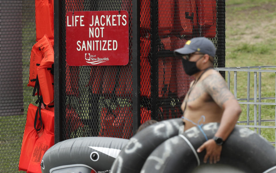 A tuber, wearing a mask to protect against the spread of COVID-19, passes a rack of life jackets as he prepares to float the Comal River, Thursday, June 25, 2020, in New Braunfels, Texas. Texas Gov. Greg Abbott said Wednesday that the state is facing a "massive outbreak" in the coronavirus pandemic and that some new local restrictions may be needed to protect hospital space for new patients. (AP Photo/Eric Gay)