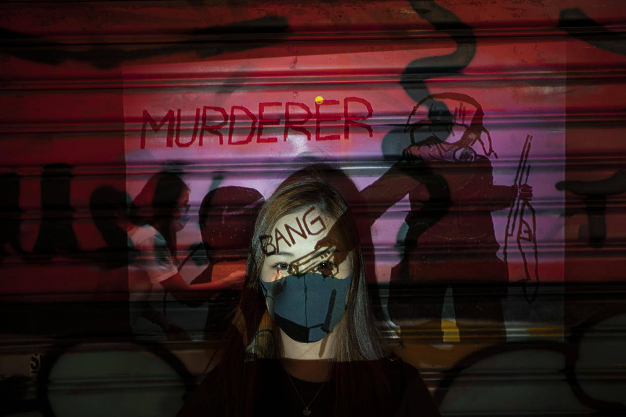 A 24-year-old protester who identified herself as Kathy, poses for a portrait as a projector displays a photograph, previously taken during the unrest, over her at a protest in Hong Kong. Police have arrested thousands of protesters since June, on charges such as illegal assembly and rioting. An attempt last month to impose a city-wide mask ban only further inflamed the demonstrators, who now cover up in defiance. (Photo: Felipe Dana/AP)