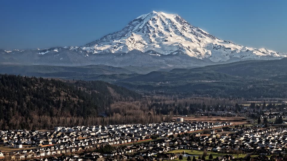 Mount Rainier, a snow-capped volcano, looms over the Puyallup Valley near Orting, Washington.  The prospect of a lahar – a fast-moving debris flow caused by melting snow and ice, typically during a volcanic eruption – poses a threat to neighboring communities.  - Ed Ruttledge/US Geological Survey Cascades Volcano Observatory