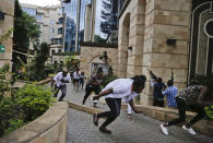 Civilians flee as security forces aim their weapons at the buildings of a hotel complex in Nairobi, Kenya, Tuesday, Jan. 15, 2019. Extremists launched a deadly attack on a luxury hotel in Kenya's capital Tuesday, sending people fleeing in panic as explosions and heavy gunfire reverberated through the complex. A police officer said he saw bodies, "but there was no time to count the dead." (AP Photo/Khalil Senosi)