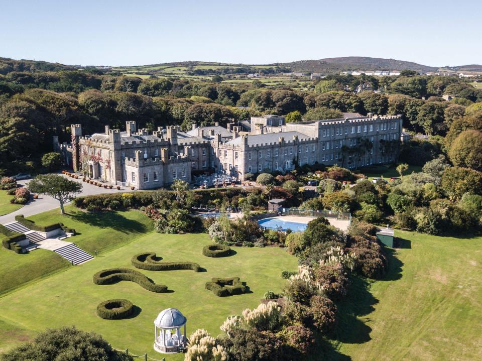 An aerial view of a stone castle surrounded by lush, greenery in Cornwall, UK.