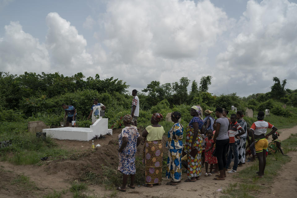 A man paints the grave stone of a relative in white, as a symbol that the soul of the deceased remains in peace, as members of the family stand by, during the Day of the Dead celebrations in Abidjan, Ivory Coast, Monday, Nov. 2, 2020. (AP Photo/Leo Correa)