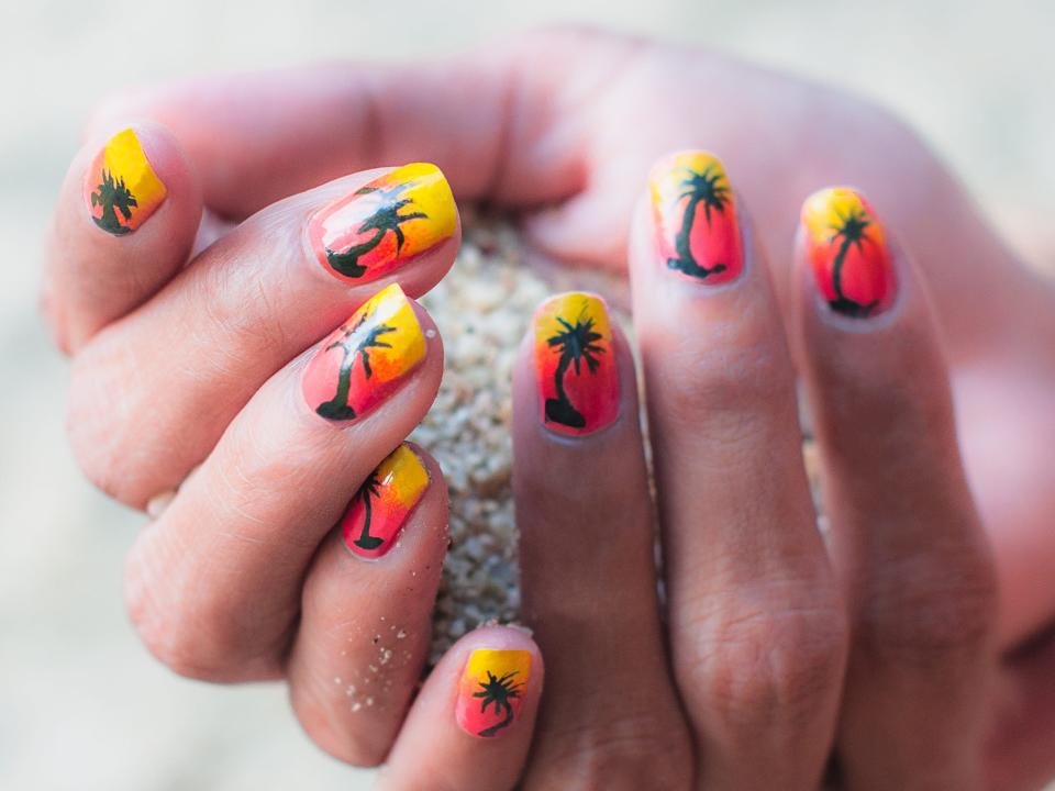 Hands with tropical sunset and palm tree manicure design.