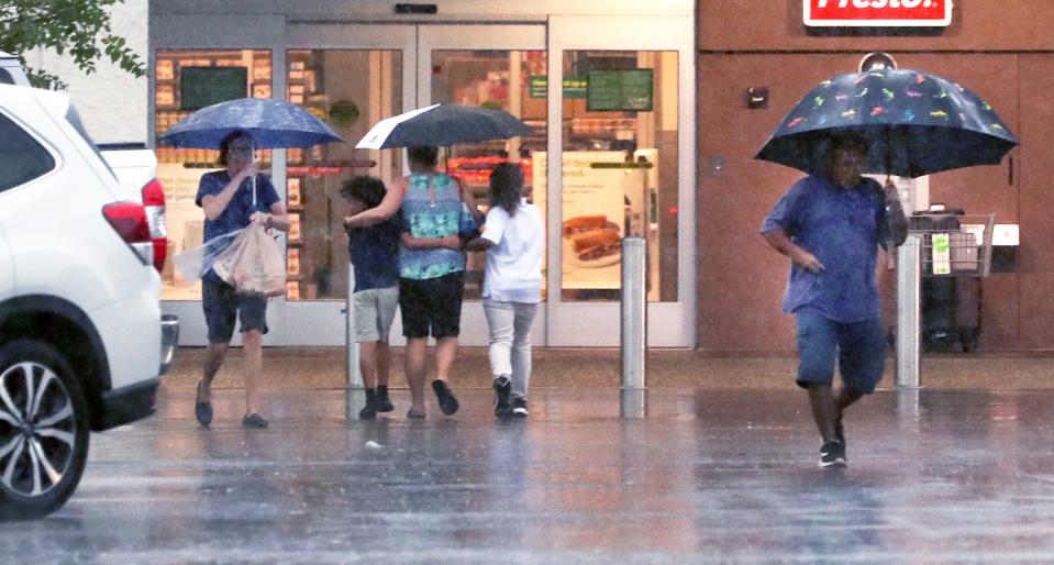 Shoppers huddle together under a umbrella in  the Trails Shopping Center parking lot in Ormond Beach recently.