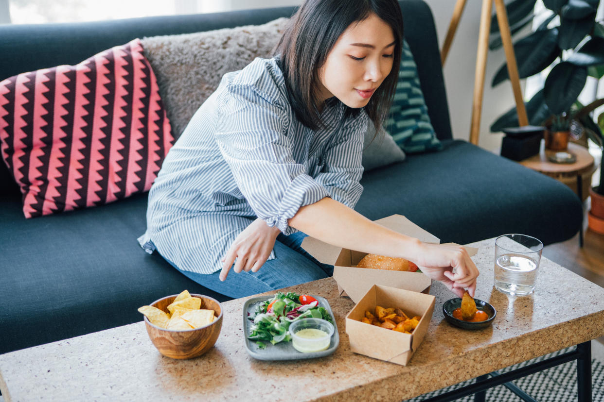 High angle view of young woman eating takeaway food, sitting on the couch at home.