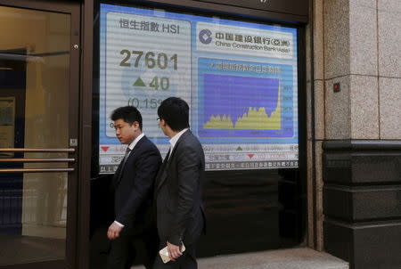 People walk past a panel displaying the benchmark Hang Seng Index during afternoon trading outside a bank in Hong Kong April 15, 2015. REUTERS/Bobby Yip