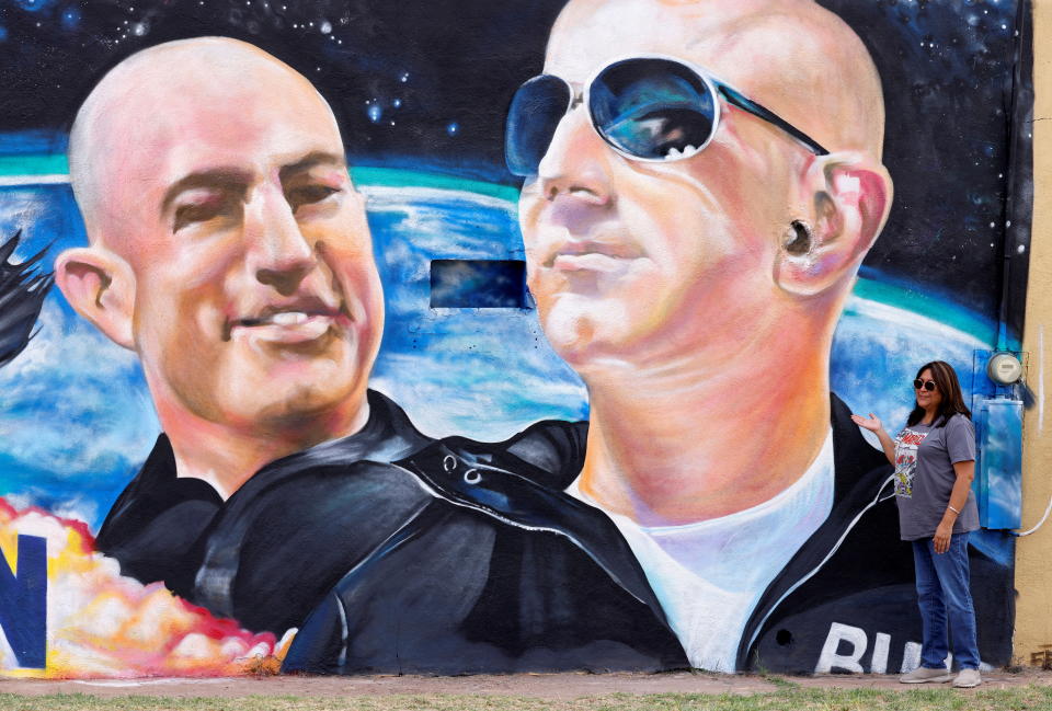 Margarita Moilina of El Paso, TX, poses next to a mural depicting billionaire American businessman Jeff Bezos (C) and his brother Mark (L) one day before their launch on Blue Origin's inaugural flight to the edge of space, in the nearby town of Van Horn, Texas, U.S. July 19, 2021.   REUTERS/Joe Skipper