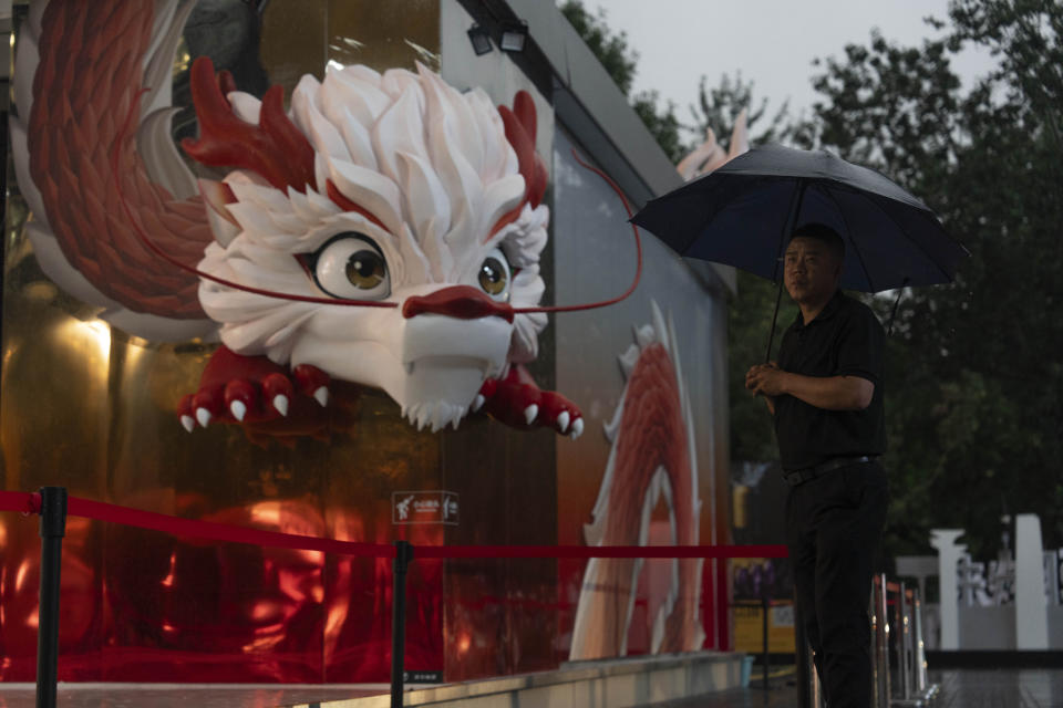 A security person stands in the rain near a depiction of a dragon at a shopping district in Beijing, July 30, 2024. (AP Photo/Ng Han Guan)