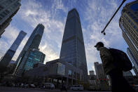 A man wearing a face mask and motorists pass through the skyscrapers at the Central Business District in Beijing, Tuesday, Nov. 24, 2020. China has reported new coronavirus cases in the cities of Shanghai and Tianjin as it seeks to prevent small outbreaks from becoming larger ones. (AP Photo/Andy Wong)