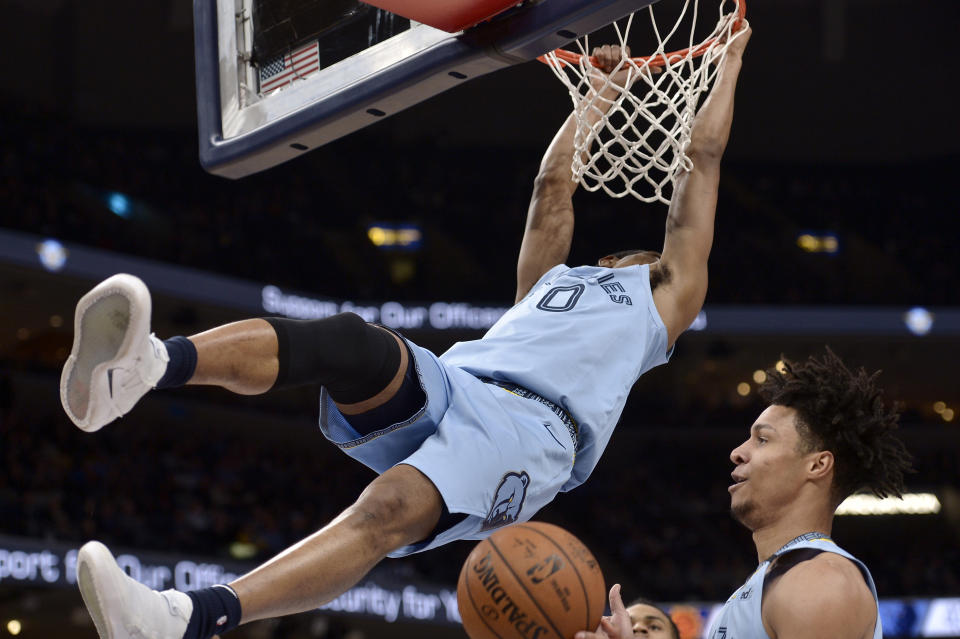 Memphis Grizzlies guard De'Anthony Melton (0) hangs from the rim after a dunk as Grizzlies forward Brandon Clarke, right, gathers the ball in the first half of an NBA basketball game against the Phoenix Suns, Sunday, Jan. 26, 2020, in Memphis, Tenn. (AP Photo/Brandon Dill)
