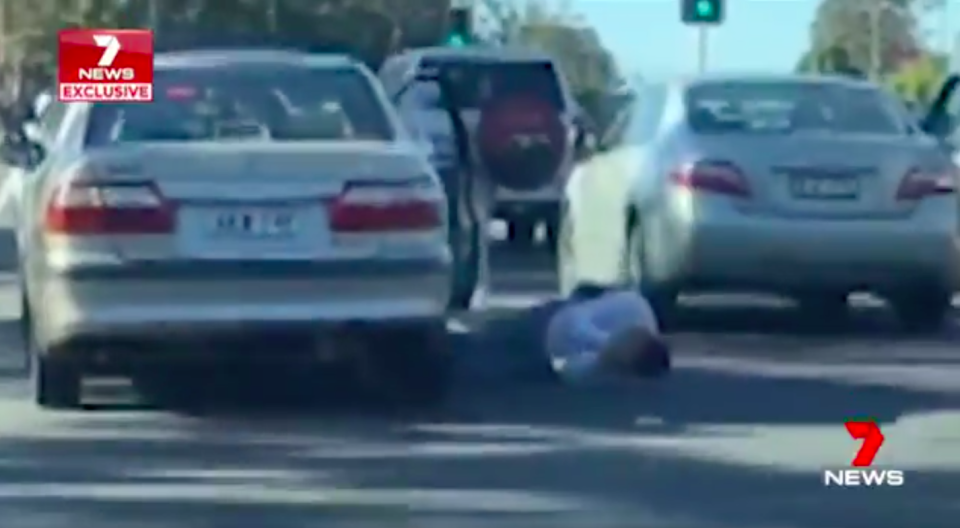 The driver opens his car and falls out onto the road, evidently injured as he clutches his head. Source: 7News