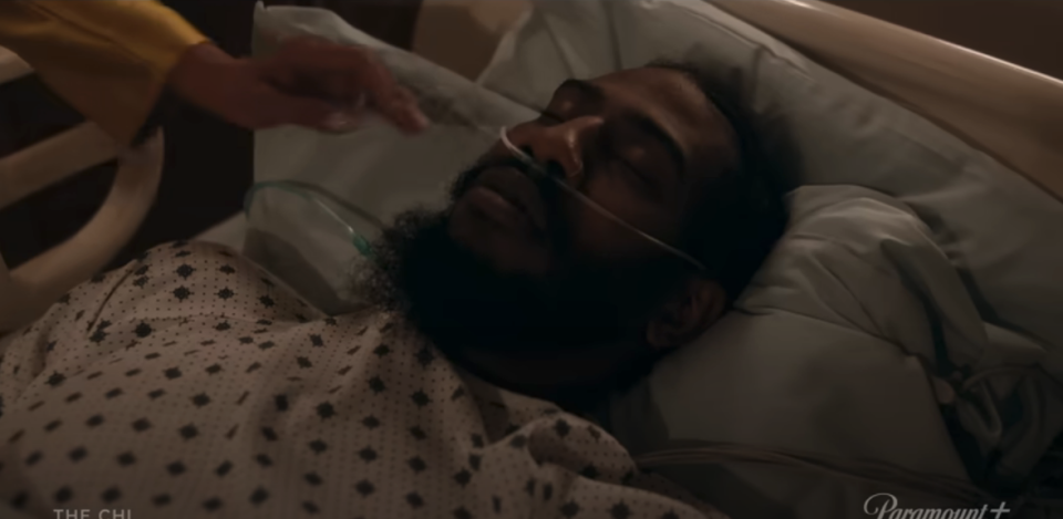 A scene from "The Chi" with a character in a hospital bed, another character reaches out to them