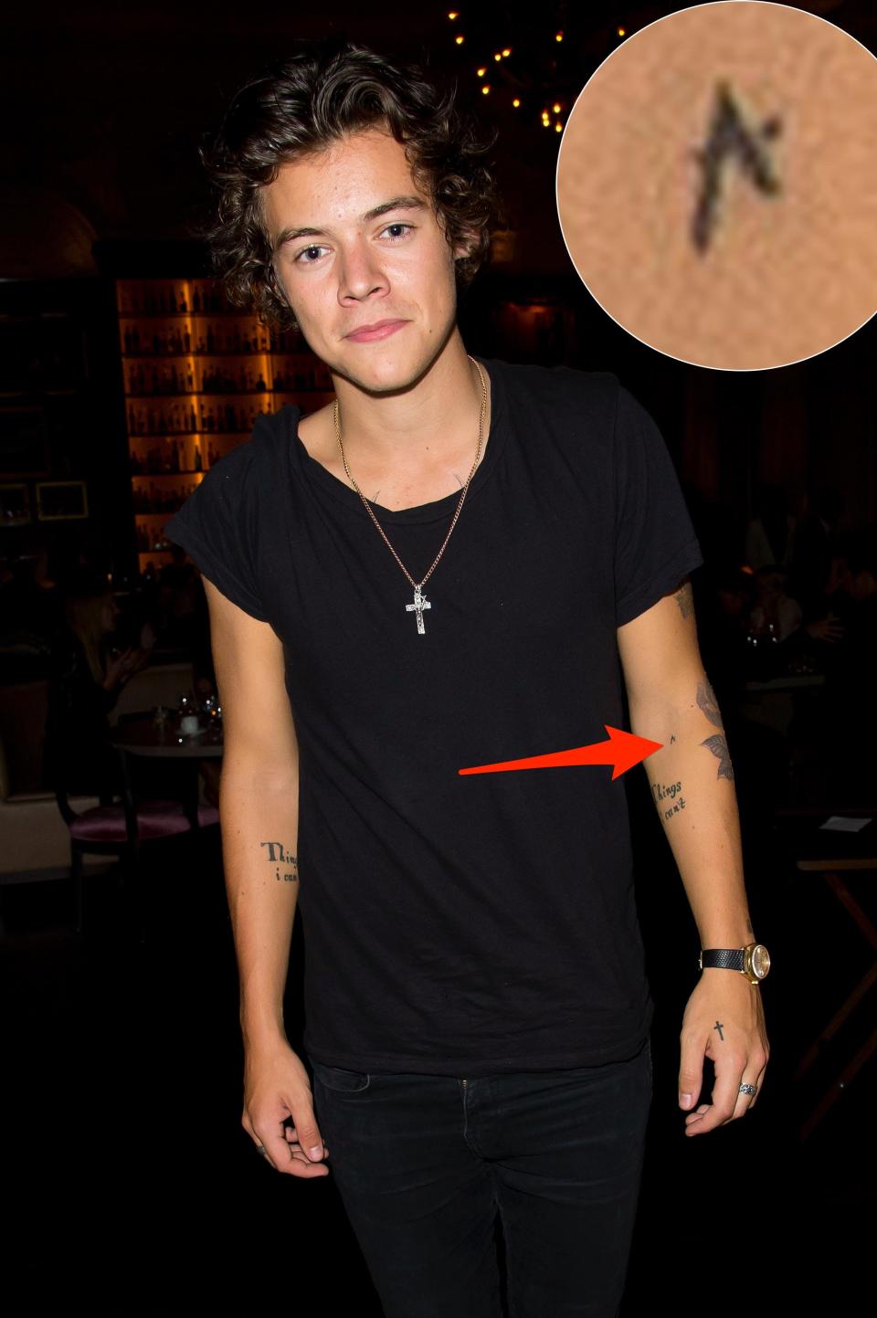 A red arrow pointing to Harry Styles' "A" tattoo on his arm.