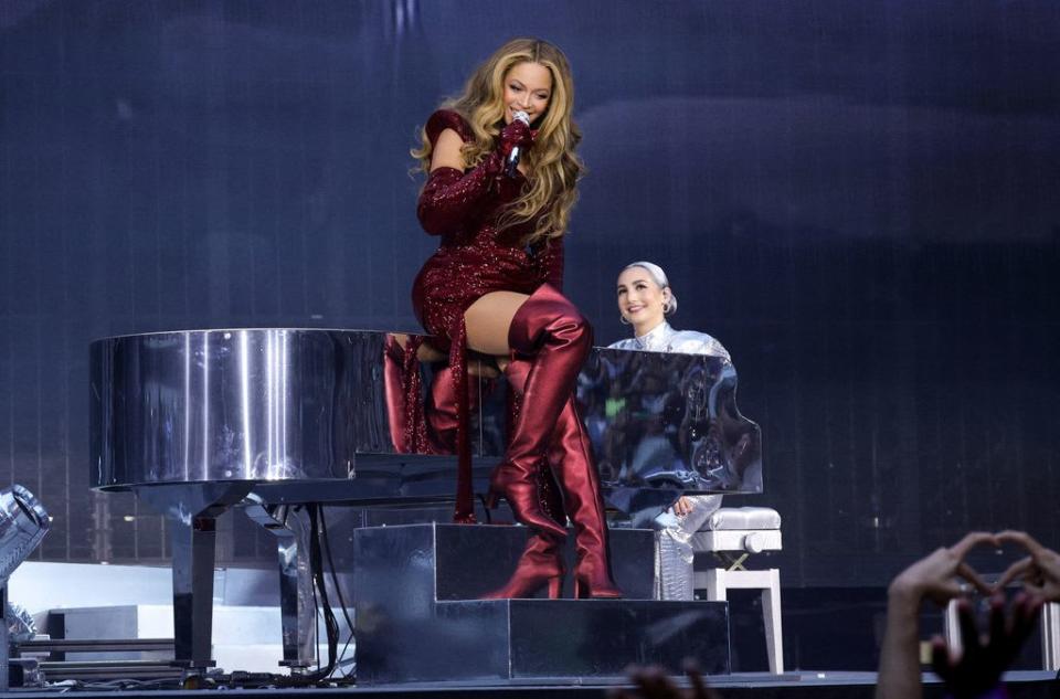 Beyoncé wears a glittering red mini dress and thigh-high boots whilst sitting on a piano