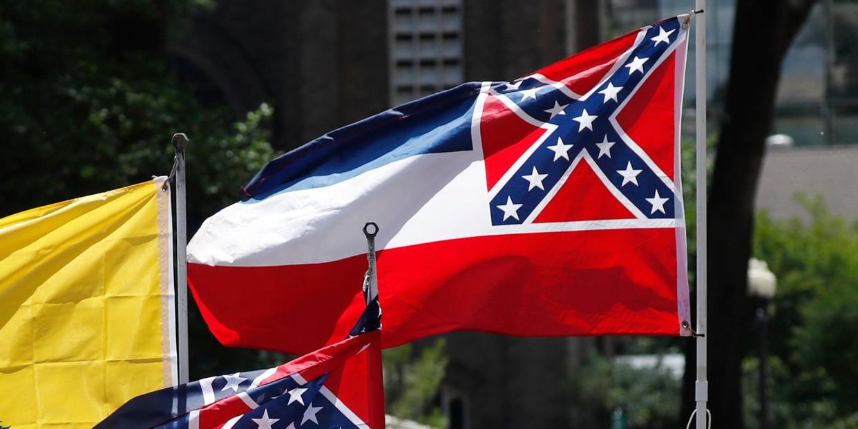 In this April 25, 2020 photo, Mississippi state flags are positioned on a vehicle amid an arrangement with the American flag and a Gadsden flag during a drive-by "re-open Mississippi" protest past the Governor's Mansion, in Jackson, Miss. There is a growing movement to replace the current state flag that has in the canton portion of the flag the design of the Civil War-era Confederate battle flag. (AP Photo/Rogelio V. Solis)