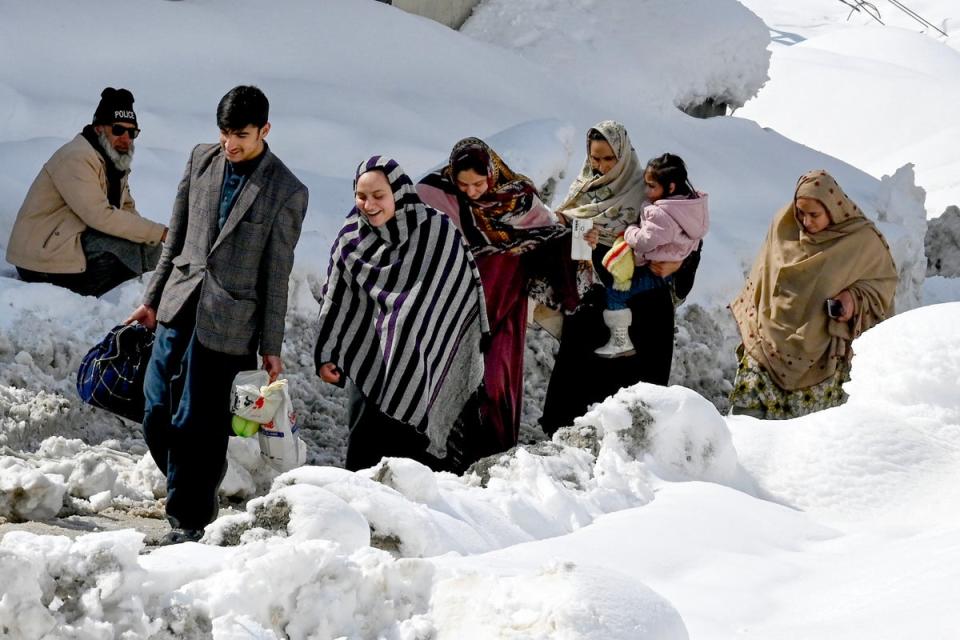 People walk amid a snow laden street in Kalam on 4 March 2024 (AFP via Getty Images)