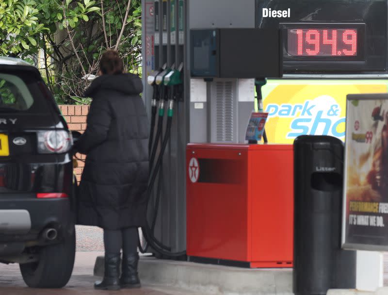 FILE PHOTO: Woman fills up her car in front of a sign showing increased fuel prices at a filling station near Liverpool