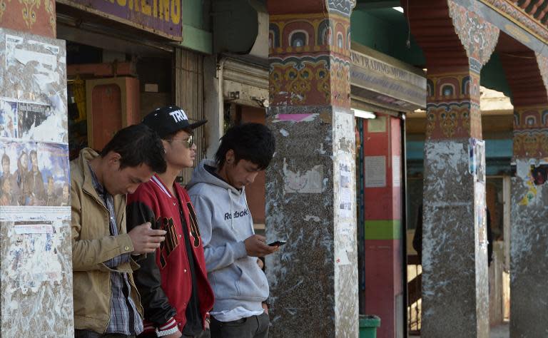 Young Bhutanese residents use mobile phones to surf the Internet as they stand on a street in the kingdom's capital Thimphu, on February 20, 2014