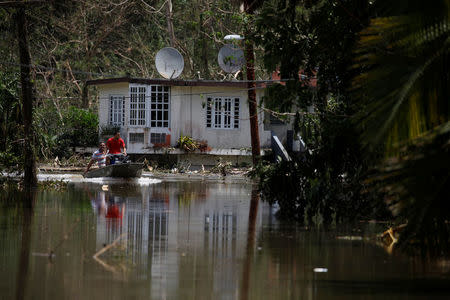Local residents use a boat to pass next to a flooded house close to the dam of the Guajataca lake. REUTERS/Carlos Garcia Rawlins