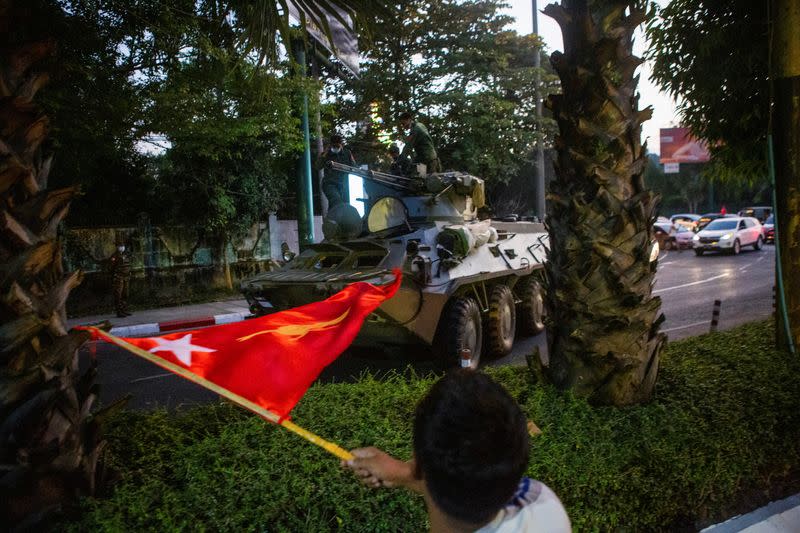 A man waves a flag next to an armoured vehicle in Yangon