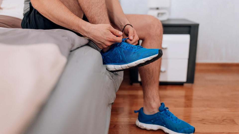 A person sitting on the edge of a bed, putting on trainers