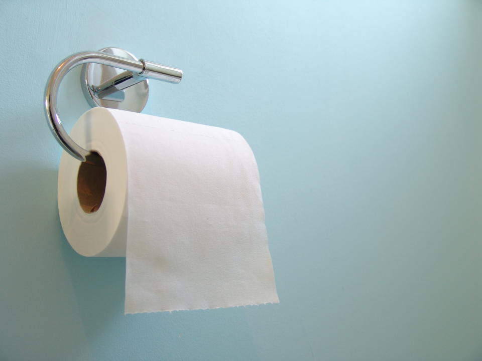 A chrome effect toilet roll holder holding toilet roll on a blue background