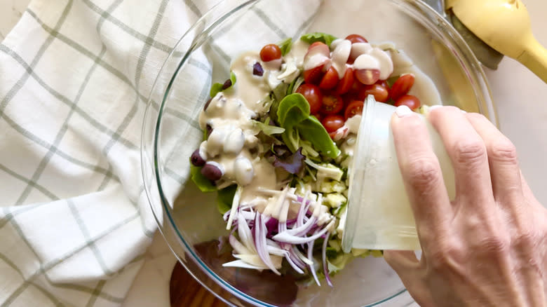 hand pouring dressing on salad