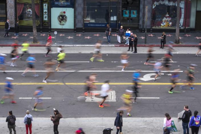 Blurred runners seen from above and to the side run along a street.
