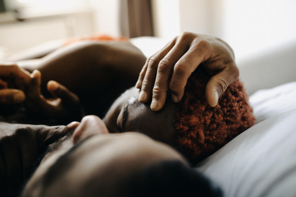 Two people embracing intimately on a bed, one caressing the other's head