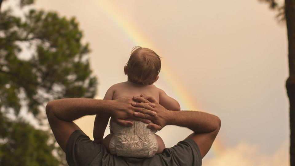 rear view father carrying son on shoulders while looking at rainbow