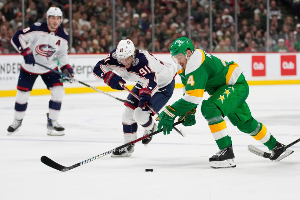 Columbus Blue Jackets center Kent Johnson (91) and Minnesota Wild defenseman Jon Merrill (4) battle for the puck during the third period of an NHL hockey game Saturday, Oct. 21, 2023, in St. Paul, Minn. (AP Photo/Abbie Parr)