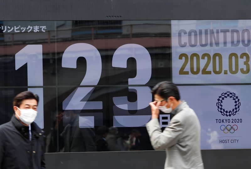 Passersby, wearing face masks due to the outbreak of the coronavirus disease (COVID-19), walk past a screen counting down the days to the Tokyo 2020 Olympic Games in Tokyo