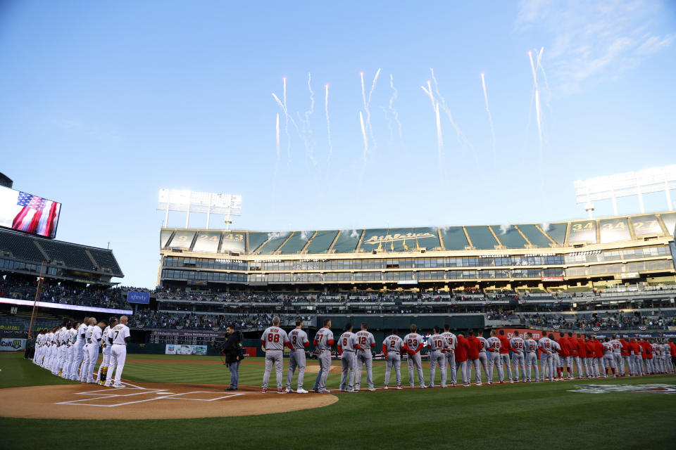 Oakland Athletics, left, and Los Angeles Angels players and coaches stand on the baselines before an opening day baseball game in Oakland, Calif., Thursday, March 30, 2023. (AP Photo/Jed Jacobsohn)