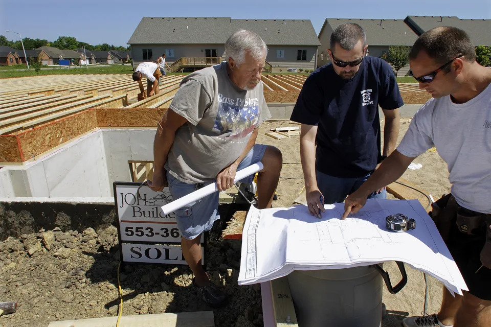 Construction workers and contractors confer over blueprints while building a new home in Springfield, Ill., (Credit: Seth Perlman, AP Photo)