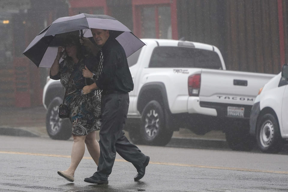 Two people cross the road as wind and rain pummel the area Friday, Sept. 9, 2022, in Julian, Calif. A tropical storm nearing Southern California has brought fierce mountain winds, high humidity, rain and the threat of flooding to a region already dealing with wildfires and an extraordinary heat wave. (AP Photo/Gregory Bull)