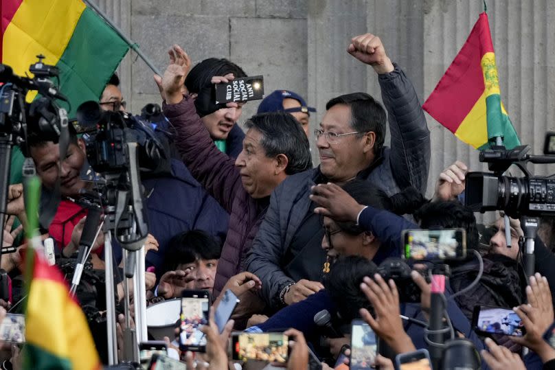 Bolivian President Luis Arce raises a clenched fist surrounded by supporters and media, outside the government palace in La Paz,