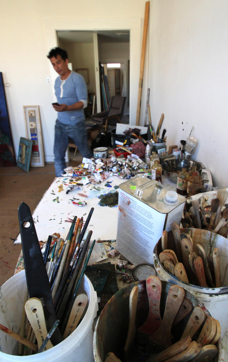 In this April 18, 2012, photo, Navajo artist Tony Abeyta walks past a table covered with brushes and paints in his studio in Santa Fe, N.M. The 46-year-old painter and jewelry designer is being honored as a "living treasure" as part of this year's Native Treasures Indian Arts Festival, which marks the start of Santa Fe's summer art season. The festival opens on May 25. (AP Photo/Susan Montoya Bryan)