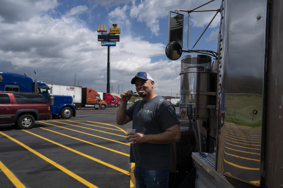 In this April 6, 2020, photo, truck driver Sammy Lloyd, of Ringgold, Ga., brushes his teeth outside his semitruck in the lot of the Love's Travel Stop truck stop in Greenville, Va.. Lloyd doesn't want brush his teeth in public restrooms during the coronavirus outbreak. He was pulling a COVID-19 emergency relief load from California to Virginia. (AP Photo/Carolyn Kaster)