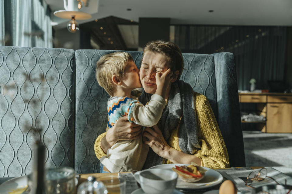 Child gives a cheek kiss to a smiling adult seated at a dining table, expressing affection