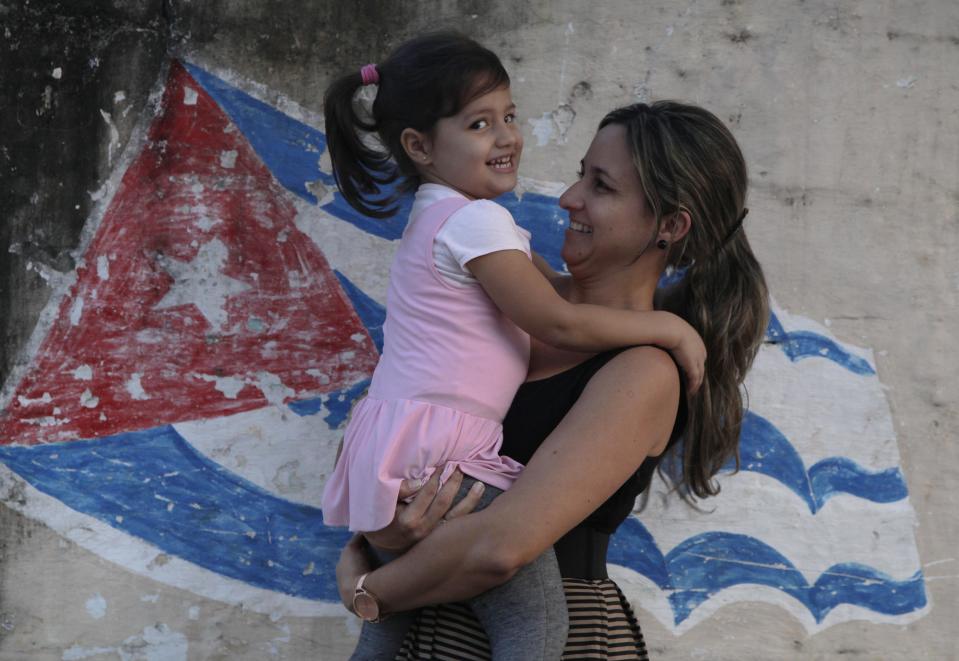 In this Feb. 19, 2014 photo, Yanitse Garcia and her daughter Olivia pose for a photo backdropped by a mural of a Cuban flag in Havana, Cuba. Garcia has spent three decades correcting people on the pronunciation and spelling of her first name. So when her firstborn came into the world three years ago, Garcia decided to save her daughter a lifetime of grief by choosing a simple name that everyone knows and which flows off the tongue: Olivia. (AP Photo/Franklin Reyes)