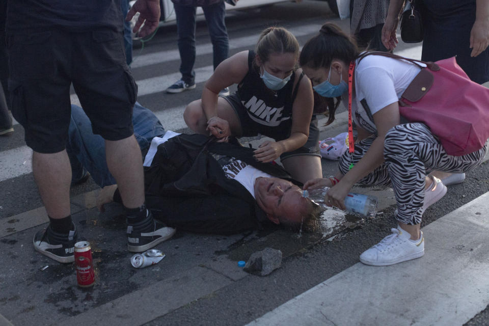 People tend to an injured man during a protest in Belgrade, Serbia, Wednesday, July 8, 2020. Police have fired tear gas at protesters in Serbia's capital during the second day of demonstrations against the president's handling of the country's coronavirus outbreak. President Aleksandar Vucic backtracked on his plans to reinstate a coronavirus lockdown in Belgrade this week, but it didn't stop people from firing flares and throwing stones while trying to storm the downtown parliament building. (AP Photo/Marko Drobnjakovic)