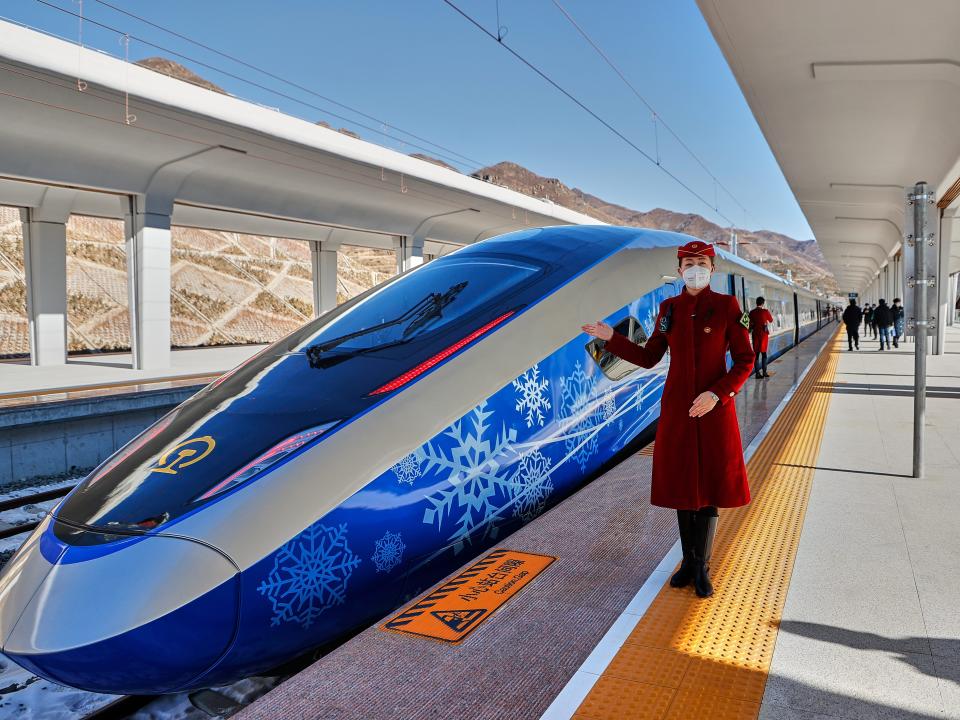 A train attendant poses beside an intelligent Fuxing bullet train decorated with a Winter Olympics-themed coating at Chongli Railway Station on January 6, 2022 in Zhangjiakou, Hebei Province of China.