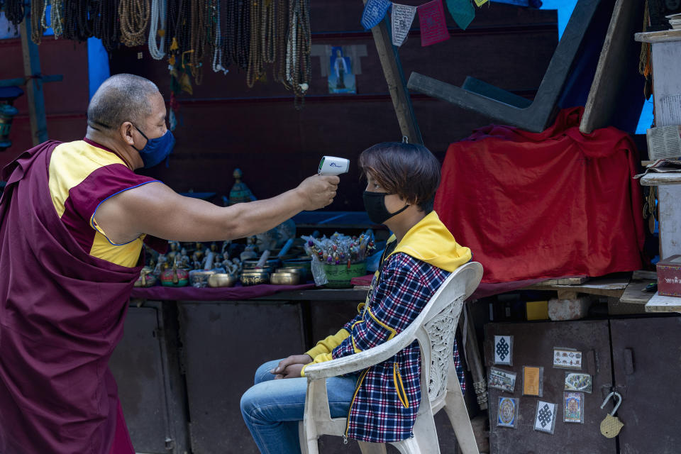 An exile Tibetan Buddhist monk uses a digital probe thermometer to measure the body temperature of a roadside vendor in Dharmsala, India, Sunday, May 24, 2020. The monk has been walking around the town for the past one week checking people's temperature as part of community service amid the COVID-19 pandemic. (AP Photo/Ashwini Bhatia)