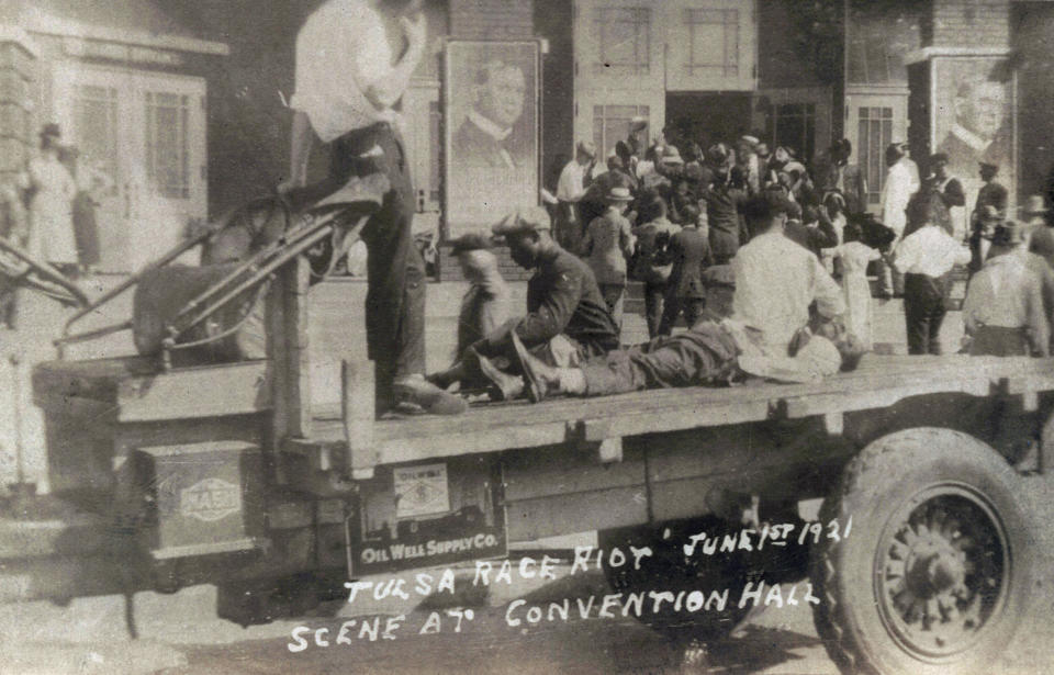 FILE - This photo provided by the Department of Special Collections, McFarlin Library, The University of Tulsa shows a truck parked in front of the Convention Hall with a Black man whose condition is unknown lying on the bed of a truck during the Tulsa Race Massacre in Tulsa, Okla., on June 1, 1921. A man in civilian clothing, left, stands guard. (Department of Special Collections, McFarlin Library, The University of Tulsa via AP, File)