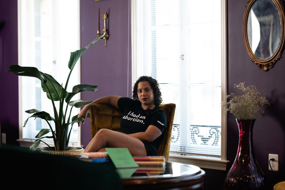 A woman sits behind a desk, wears a shirt that says "I had an abortion."