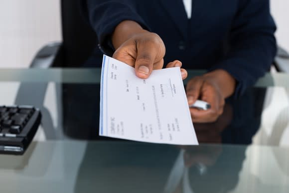 Person holding out a check over a table.