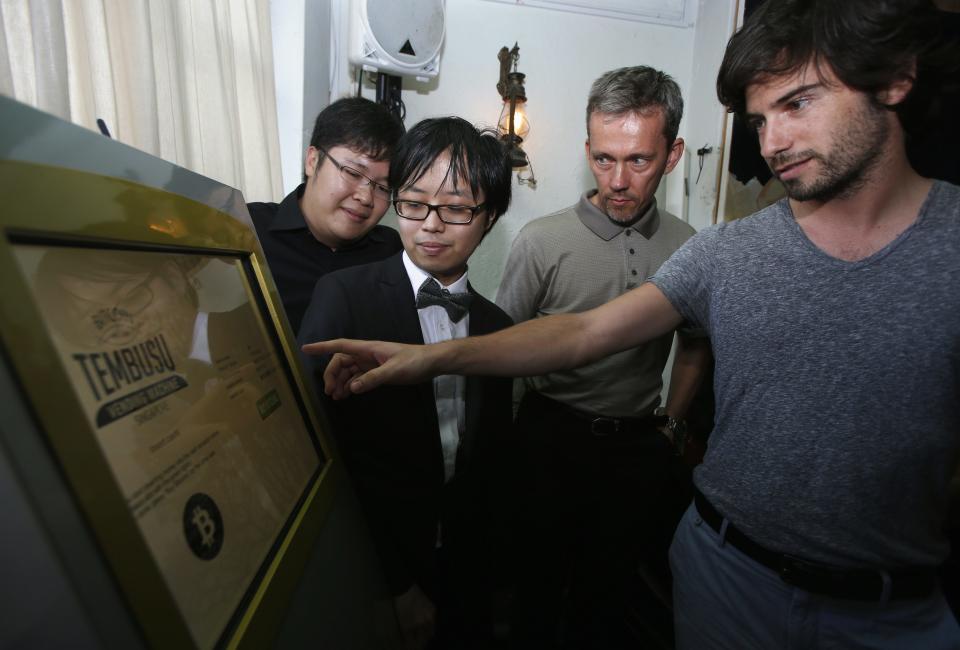 Tembusu Terminals' partners (back L-R) Jarrod Luo, Peter Peh Sik Wee and Andras Kristof watch as a volunteer demonstrates the use of their Bitcoin vending machine during a launch at a pub in Singapore February 27, 2014. According to Tembusu Terminals, this is the first Bitcoin vending machine in Asia. REUTERS/Edgar Su