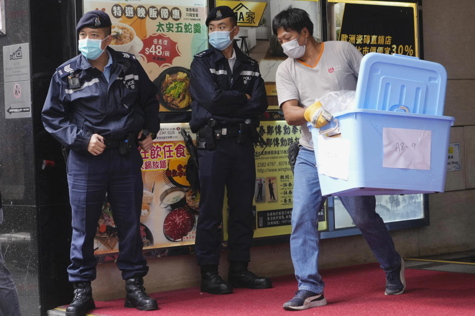 A worker carrying some containers walks past police officers outside the office of Stand News in Hong Kong, Wednesday, Dec. 29, 2021. Hong Kong police raided the office of the online news outlet on Wednesday after arresting several people for conspiracy to publish a seditious publication. (AP Photo/Vincent Yu)