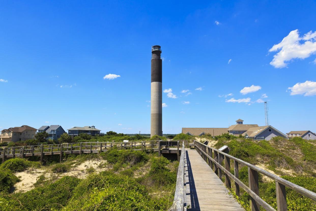 lighthouse standing tall over boardwalk and homes